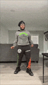 a man in a gray hoodie and black sweatpants is standing in front of a couch
