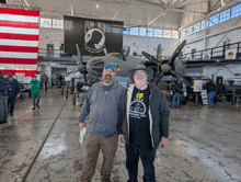 two men standing in front of an airplane with a pow mia banner hanging on the wall