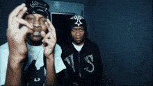 a man wearing a black hoodie with the letter s on it stands next to another man