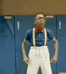 a man wearing glasses and suspenders is standing in front of a blue wall .