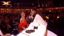 a woman in a red dress is sitting next to a man holding a microphone on a stage