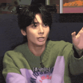 a young man wearing a green and purple sweater with korean writing on the front