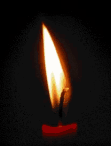 a red candle with a single flame is lit up in the dark