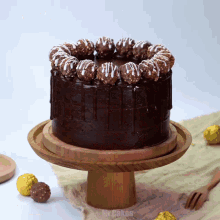 a chocolate cake with ferrero rocher balls on top is on a wooden stand