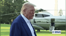 a man in a blue suit stands in front of a united helicopter
