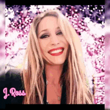 a woman with long blonde hair and red lips is smiling in front of a pink background with flowers .