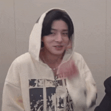 a young man wearing a white hoodie is covering his mouth with his hand .