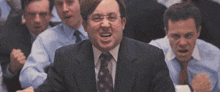 a man in a suit and tie is sitting in front of a group of men .