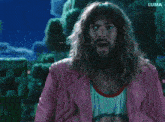 a man with long hair and a beard is standing in front of a green monster and the word luma is on the bottom
