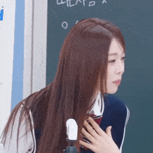 a woman in a school uniform holds her hand to her chest in front of a blackboard with the letter o written on it