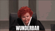 a judge with red hair and glasses is sitting in a courtroom with the word wunderbar written on the screen behind her .