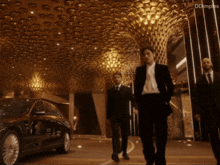 three men in suits and ties are walking in front of a car and a building that says dolimpiades