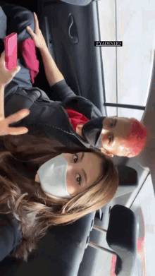 a man and a woman wearing face masks in a car with a sticker that says " adinho "