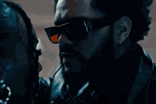 a man wearing sunglasses and a leather jacket looks at a woman