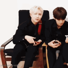 two young men are sitting in chairs and one of them is pointing at his phone