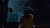 a man and a woman are looking at a skeleton that is flying over a burning house