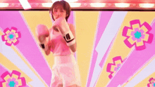 a woman in a pink top and white shorts is boxing in front of a pink and yellow background with flowers