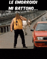 a man in a yellow tank top is walking down a street next to a red car with the caption le emorroidi mi battono