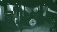 a man playing a guitar in a dark room with a drum set in the background