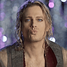 a man with long blonde hair blowing a kiss at the camera