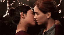 a couple of women are kissing each other in front of a string of lights .