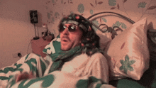 a man laying on a bed wearing sunglasses and a scarf with the letter r on it