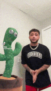 a man is standing next to a stuffed green cactus .