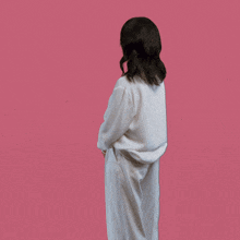 a woman in a white shirt and white pants is standing with her arms outstretched on a pink background