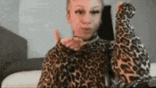 a woman in a leopard print sweater is sitting on a bed and holding a cell phone .