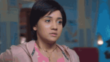 a close up of a woman 's face with a pink jacket and a gold necklace