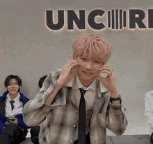 a man with pink hair is sitting in front of a sign that says uncire