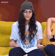 a woman wearing a beanie and glasses is sitting on a couch with a guitar ..