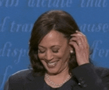 a woman in a suit and pearls is smiling and touching her hair