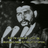 a man speaking into a microphone with the words " and the statue of lumumba destroyed today but rebuilt tomorrow " visible