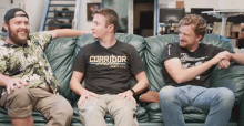three men are sitting on a couch and one of them is wearing a corridor digital shirt .