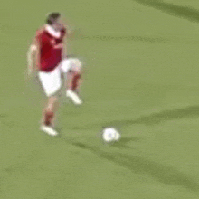a man in a red shirt and white shorts is playing soccer on a field .