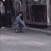 a woman is squatting down on the sidewalk in front of a train