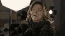 a woman wearing a black sweater and gloves is laughing with her eyes closed