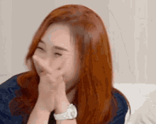 a woman with red hair is laughing with her hands covering her mouth .