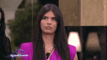 a woman in a pink shirt is standing in front of a mirror and a sign that says grandefratello