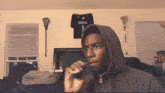 a man in a hoodie smoking an electronic cigarette in a bedroom