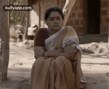 a woman in a saree is sitting on the ground with her arms around her waist .