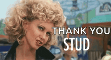 a woman with curly blonde hair is standing in front of a sign that says thank you stud .