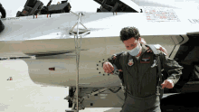 a man wearing a mask stands in front of a fighter jet with the word officer on it