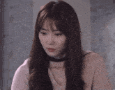 a woman with long hair and a choker looks down
