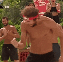 a shirtless man wearing a red headband is dancing in front of a group of people