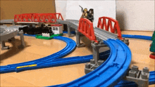 a toy train set is sitting on a wooden floor with a red bridge .