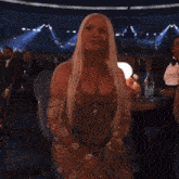 a woman with long blonde hair is standing in front of a crowd of people .