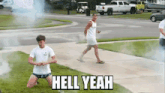 a man is kneeling down in the grass with smoke coming out of his mouth while another man walks down the sidewalk .