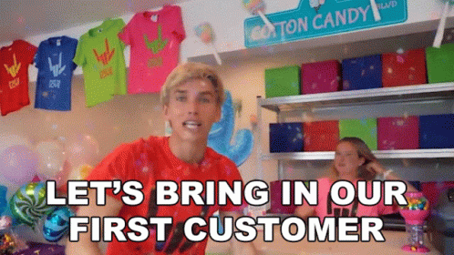 Man in red shirt with text 'LET'S BRING IN OUR FIRST CUSTOMER' in a colorful room